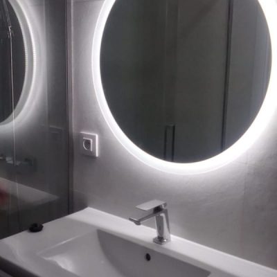 Espejo redondo retroiluminado y lavabo moderno en un baño minimalista tras una reforma de baños en Sevilla.